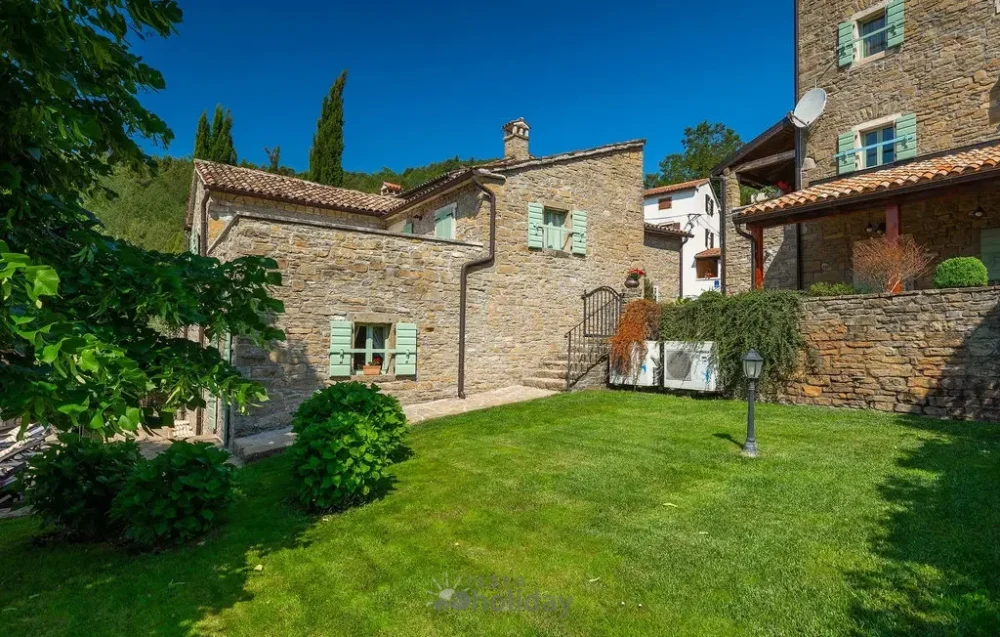 Rustic stone house with green shutters and lawn.