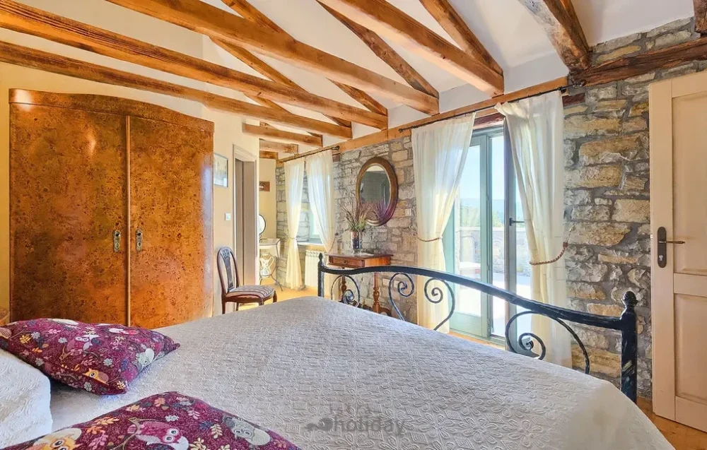Rustic bedroom with stone walls and wooden beams.