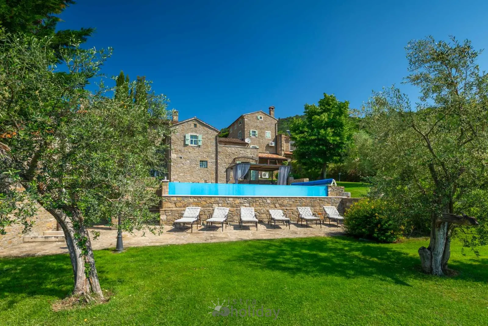 Stone villa with pool and sun loungers in garden.