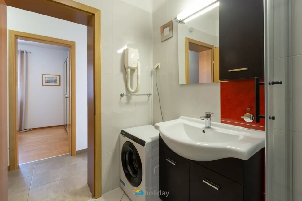 Modern bathroom with sink, washer, and red accent
