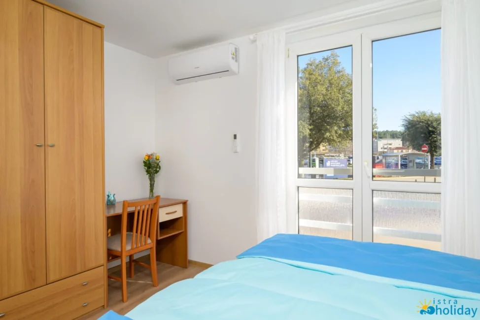 Bright bedroom with desk, window, and wardrobe.
