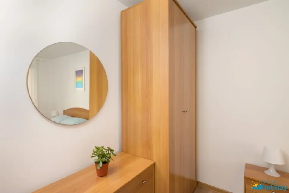 Bedroom with mirror, wooden dresser, and plant.