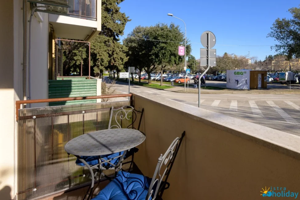 Sunny balcony overlooking a street and parking lot.