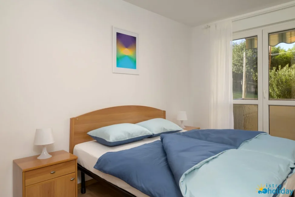 Modern bedroom with blue bedding and window view.
