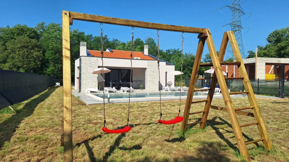 Wooden backyard swing set near modern house and pool